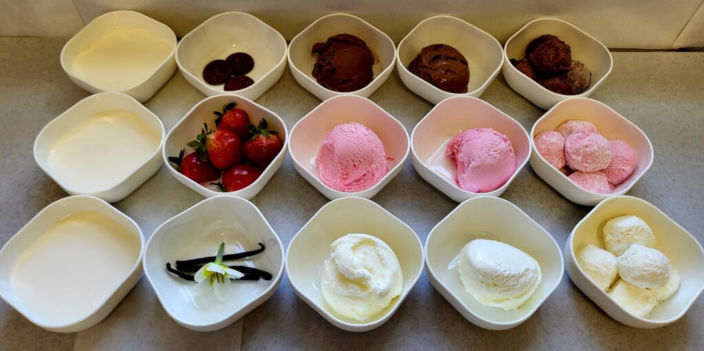 Déclinaison de crème glacée en textures adaptées et formats manger-main à la fraise, au chocolat et à la vanille, présentée dans des bols blancs.